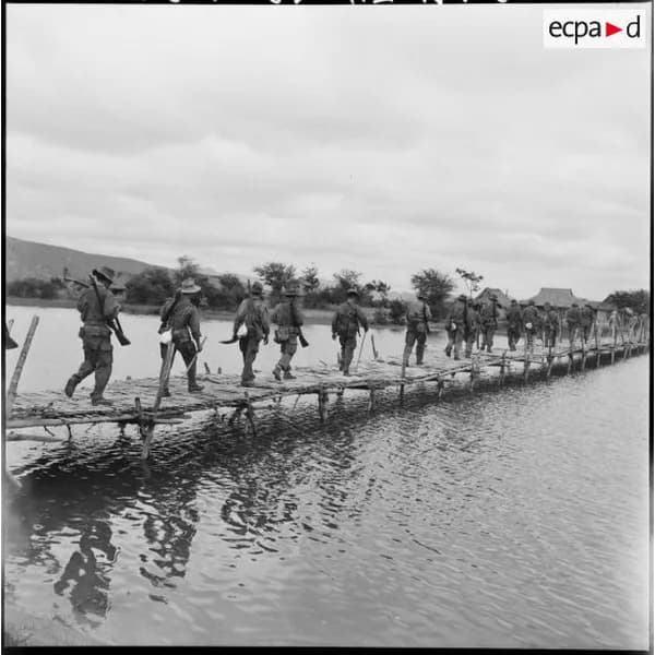 Une colonne de soldats franchit une passerelle sur l'eau